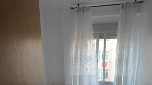 A bedroom with a bed, a wooden chair, a small table, and a window with curtains.