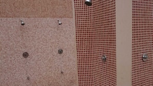 A shower area with tiled walls and floor, featuring multiple showerheads and a control panel.