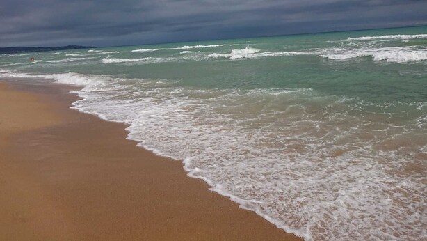 A beach with waves approaching the shore under a cloudy sky.