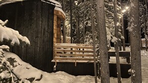 A wooden cabin with a wooden deck, surrounded by snow-covered trees. - Black Spruce - Red Door  (Whitehorse)