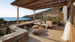 A covered outdoor seating area with stone walls, a sofa, and ottomans. - Kea Retreat (Kea)