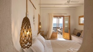 A bedroom with a bed, a hanging light fixture, a wooden door leading to a balcony, and a view of the sea. - Kea Retreat (Kea)