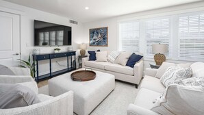 A modern living room with a white sofa, a coffee table, and a TV mounted on the wall.