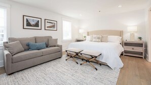 A modern bedroom with a bed, a sofa, a small table, and a nightstand.