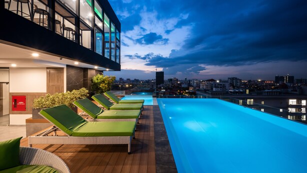 Un área de piscina en la azotea con sillones de descanso y vistas panorámicas de la ciudad al anochecer.