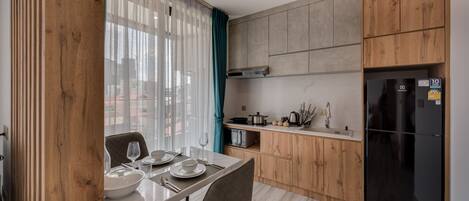 A modern kitchen with wooden cabinets, a black refrigerator, and a dining area with a table set for two.