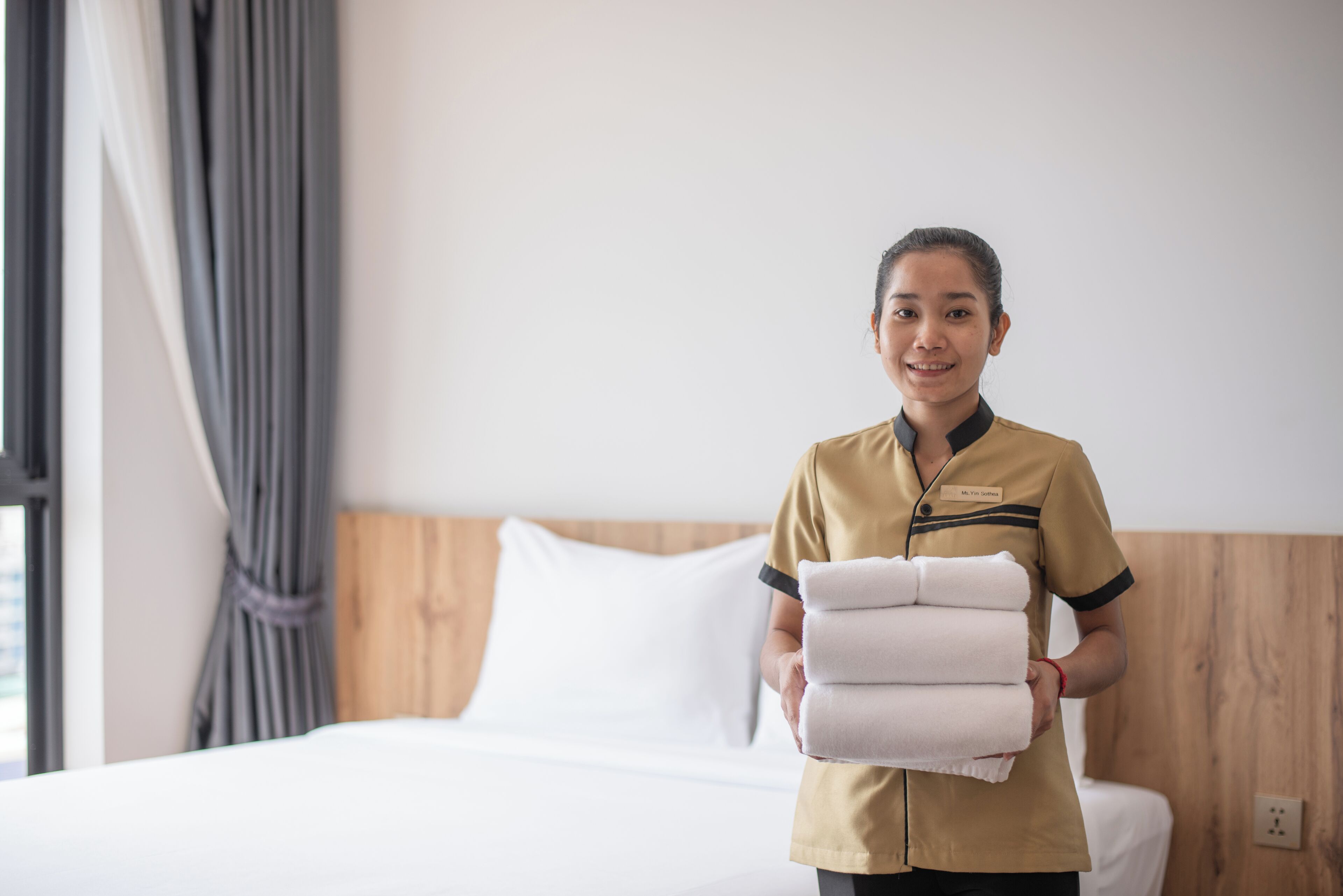Ein Hotelzimmer mit einem ordentlich bezogenen Bett, einem Holz-Kopfteil und einem Fenster mit Vorhängen.