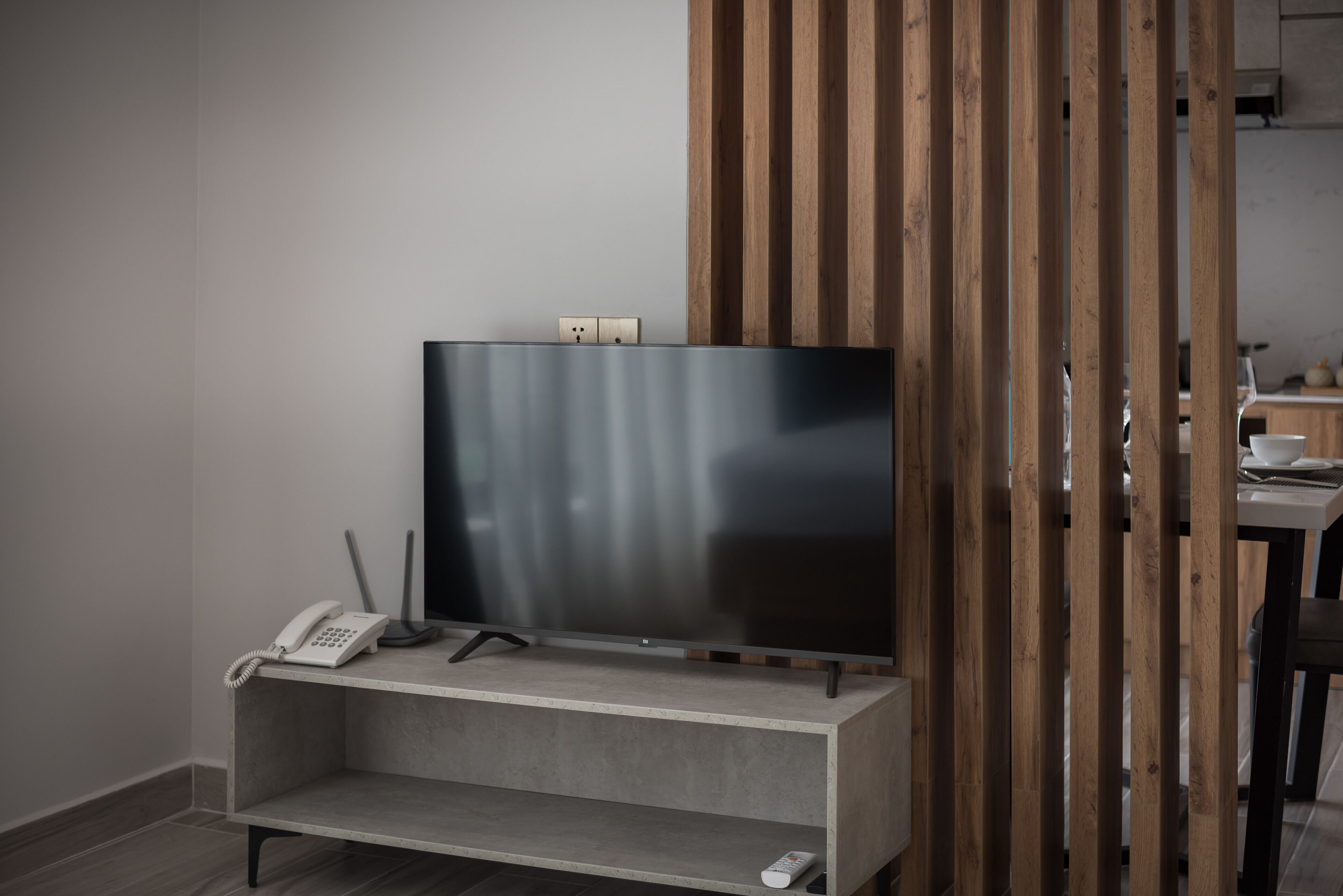 A modern room with a flat-screen TV on a wooden stand, a telephone, and a remote control on a low shelf.