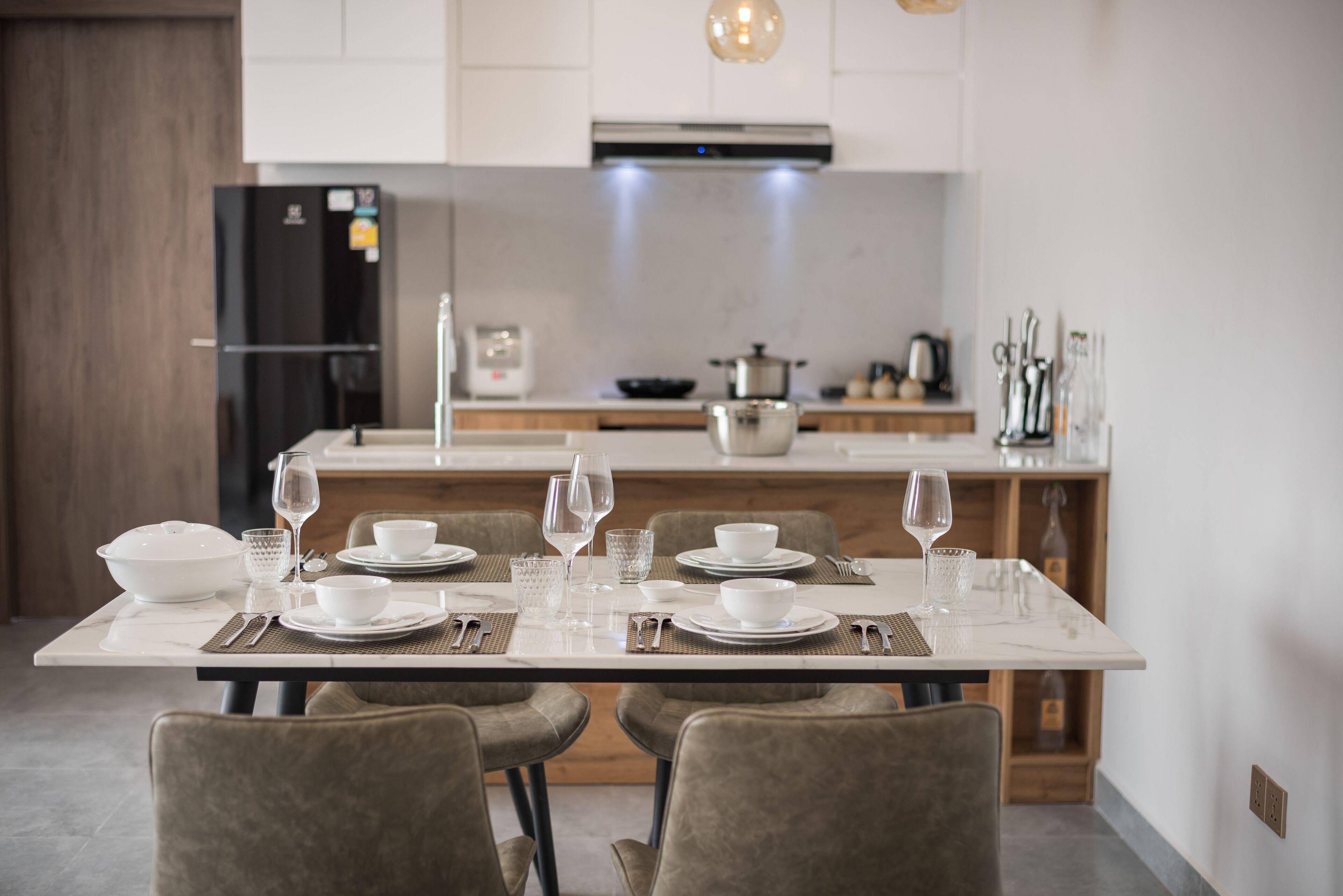 Uma cozinha moderna com armários brancos, uma geladeira preta e uma mesa de jantar posta para quatro pessoas.