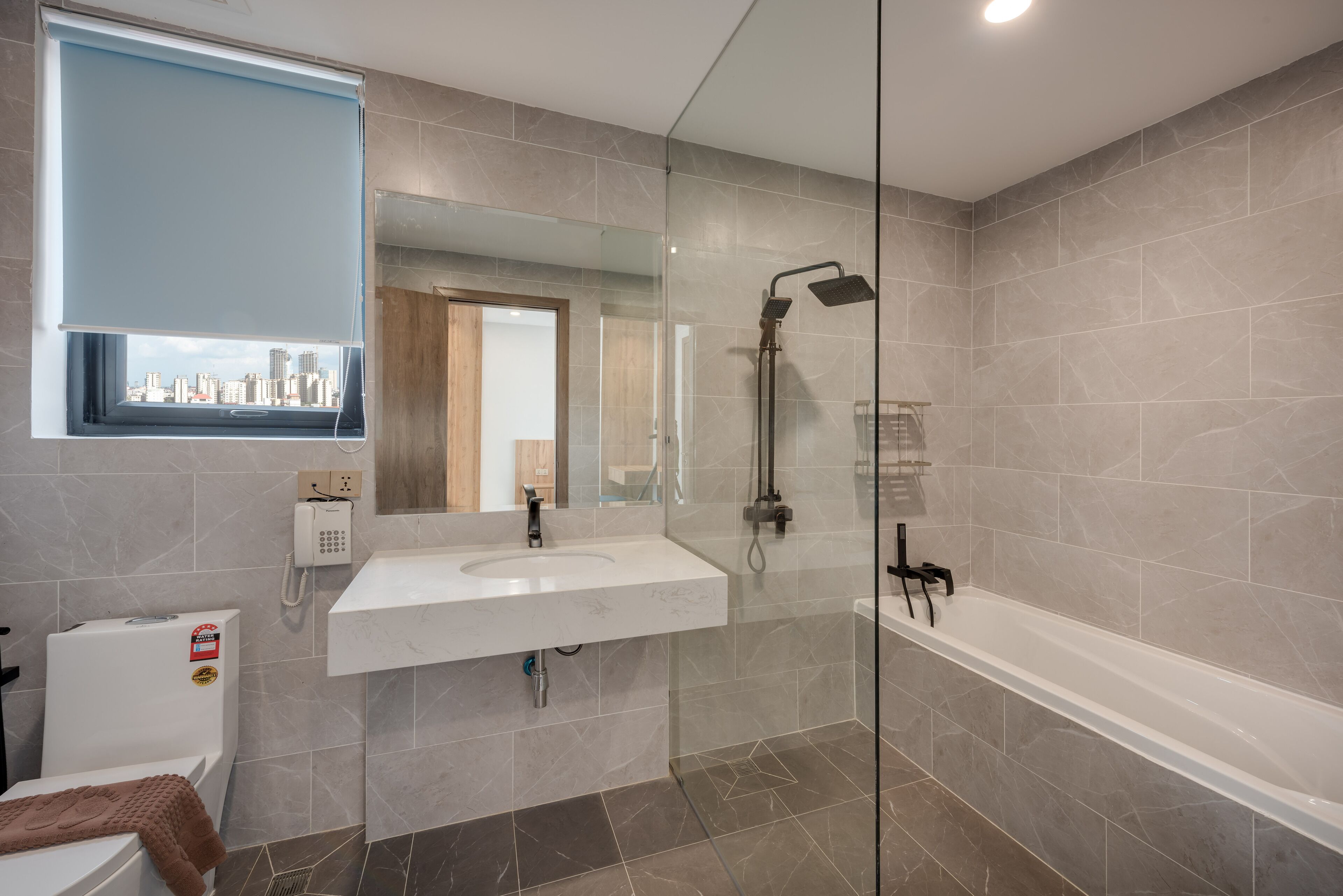 A modern bathroom with a glass-enclosed shower, a large mirror, and a city view through a window.