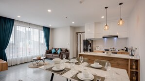 Una sala de estar moderna con comedor listo para una comida, una cocina con electrodomésticos de acero inoxidable y vistas de la ciudad a través de amplios ventanales.
