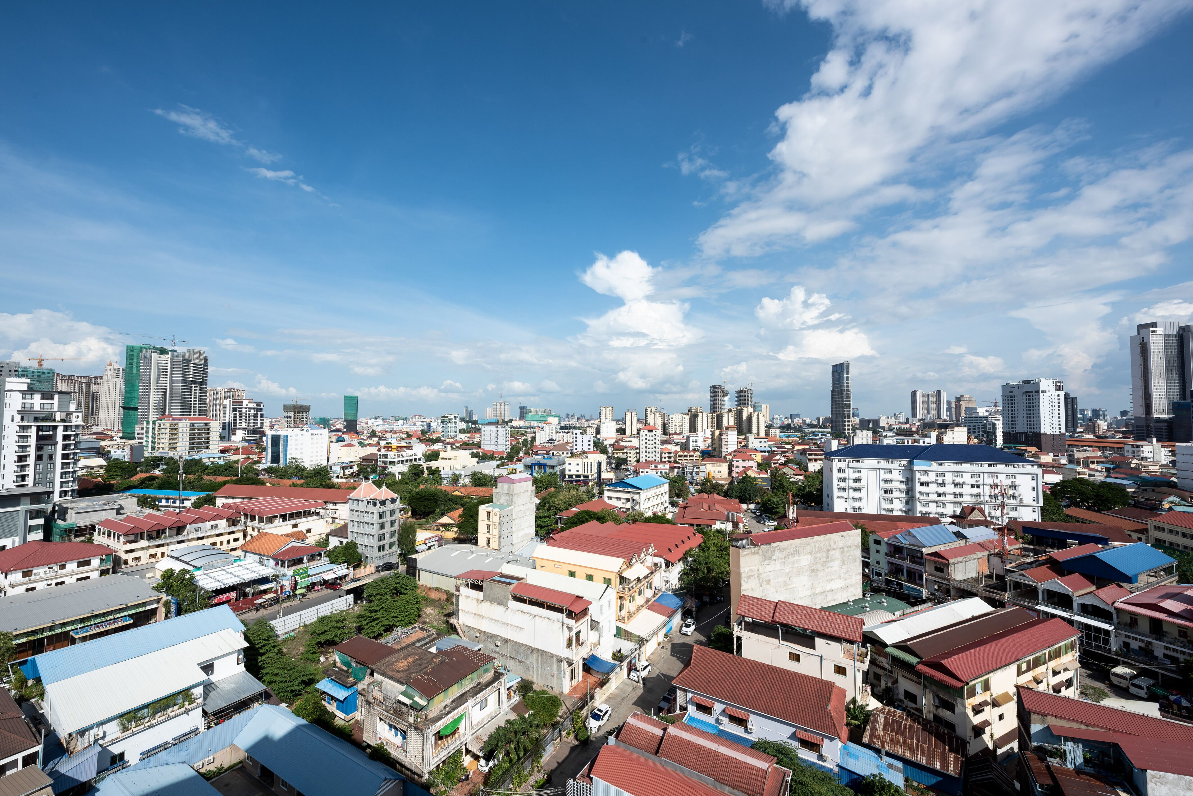 A cityscape with a mix of residential and commercial buildings, including high-rise structures and smaller houses with red roofs.