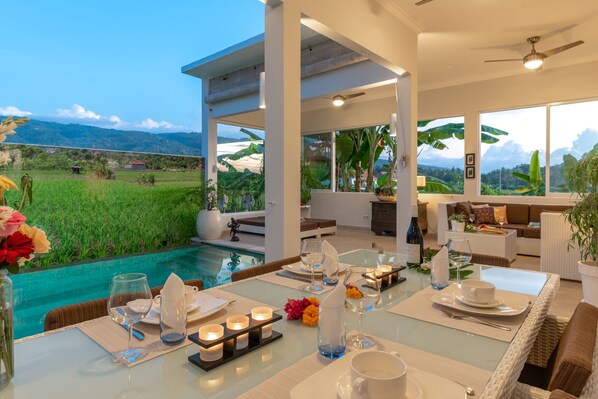 Enjoy a meal with a view of lush green landscapes and distant mountains from this dining area with a glass table and comfortable seating.