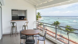 A balcony with a view of the ocean, a dining table with chairs, and a window with a shelf. - Only 4 View Rooftop Centre Sainte Anne (sainte anne)