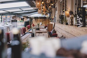 An outdoor seating area with wooden tables and benches, overhead hanging lights, and a view of the street. - Der Gollinger (Saalbach-Hinterglemm)