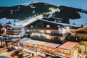A hotel with multiple floors, a ski slope in the background, and a variety of shops and restaurants on the ground floor. - Der Gollinger (Saalbach-Hinterglemm)