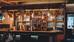 Zona de bar con estantes llenos de botellas de licor, vasos y una máquina de café.