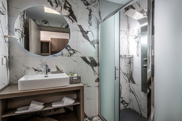A modern bathroom with a marble sink, a large mirror, and a glass-enclosed shower.