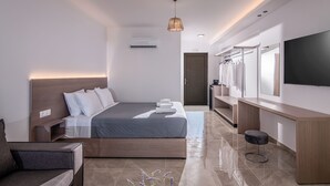 A modern hotel room with a large bed, a bedside table, a TV, and a seating area. - Ebenus Suites by Checkin (Hersonissos)