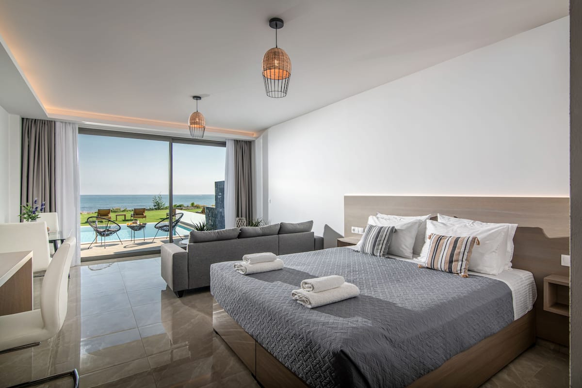Una habitación de hotel moderna con una cama grande, un sofá, un escritorio y vistas al océano.