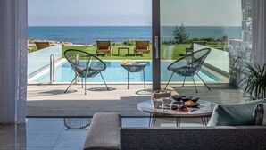 A balcony with a pool, two chairs, a table with drinks, and a view of the sea. - Ebenus Suites by Checkin (Hersonissos)