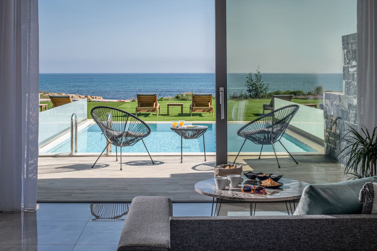 Un balcón con piscina, dos sillas, una mesa con bebidas y vista al mar.