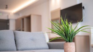 A modern living room with a grey sofa, a round coffee table, and a potted plant. - Ebenus Suites by Checkin (Hersonissos)