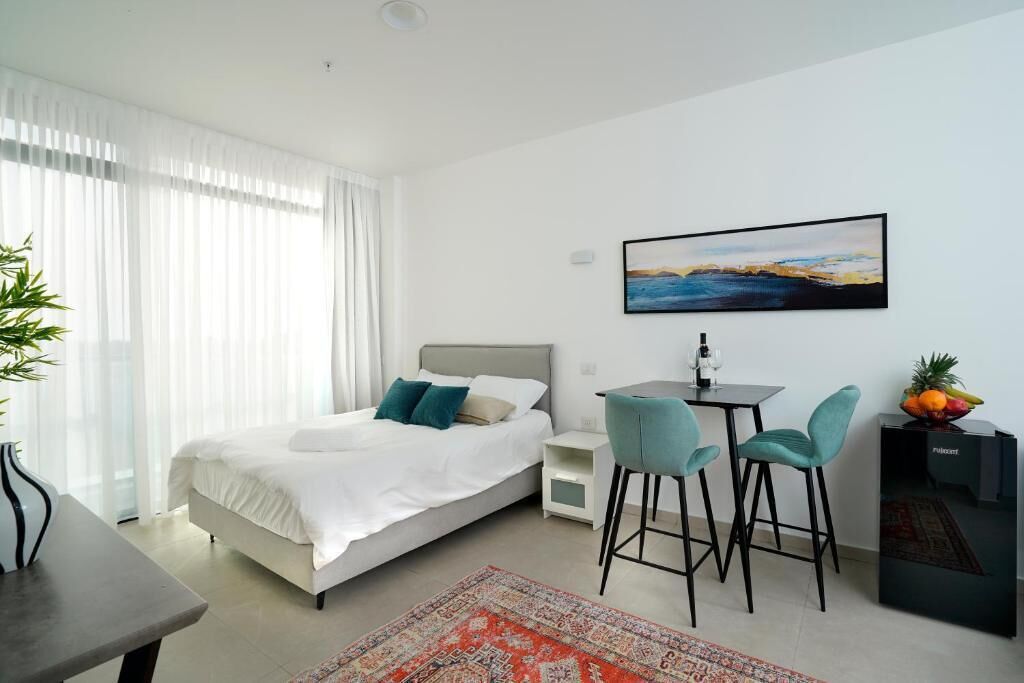 Een moderne hotelkamer met een bed, een bureau met twee stoelen, een klein tafeltje met een glas en een schaal fruit.