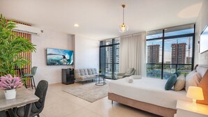 Ein modernes Hotelzimmer mit einem großen Bett, einem Essbereich, einer Couch, einem Fernseher und Blick auf die Stadt.