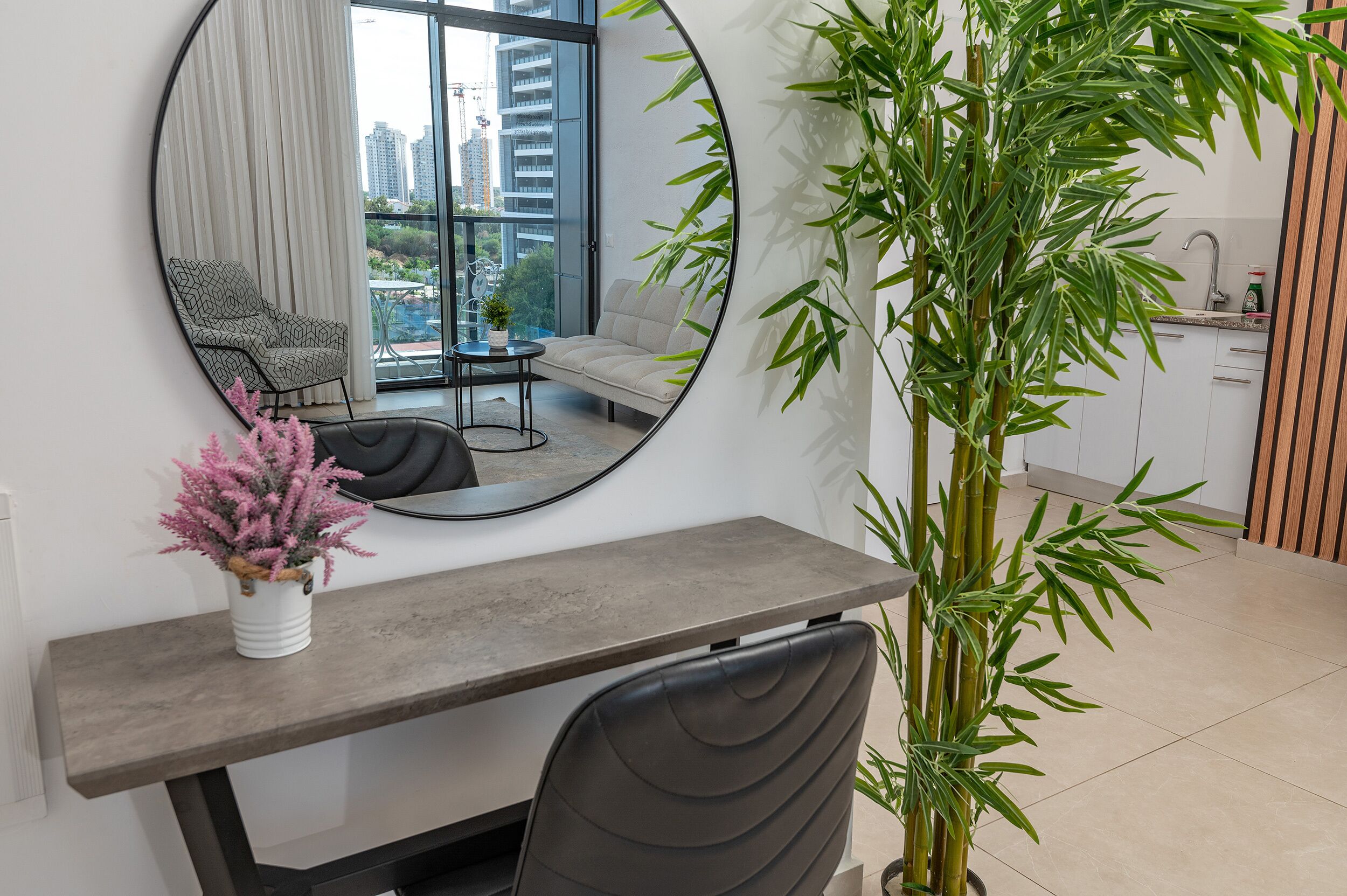 Une pièce moderne avec un grand miroir rond, une table à manger, un canapé et une grande plante en bambou.