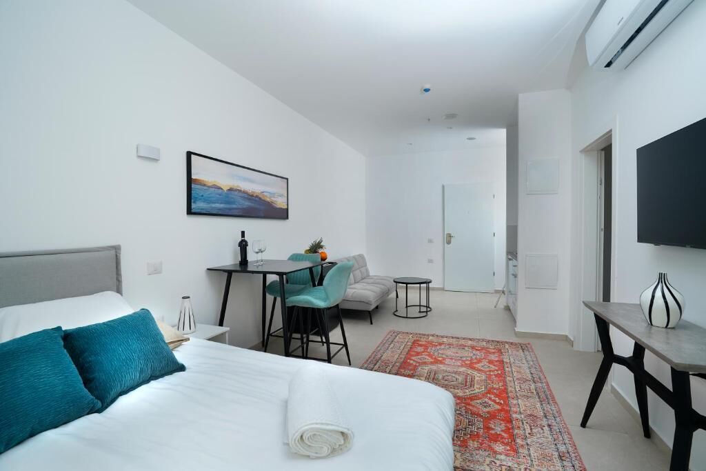 A modern hotel room with a bed, a desk, a chair, a TV, and a small table.