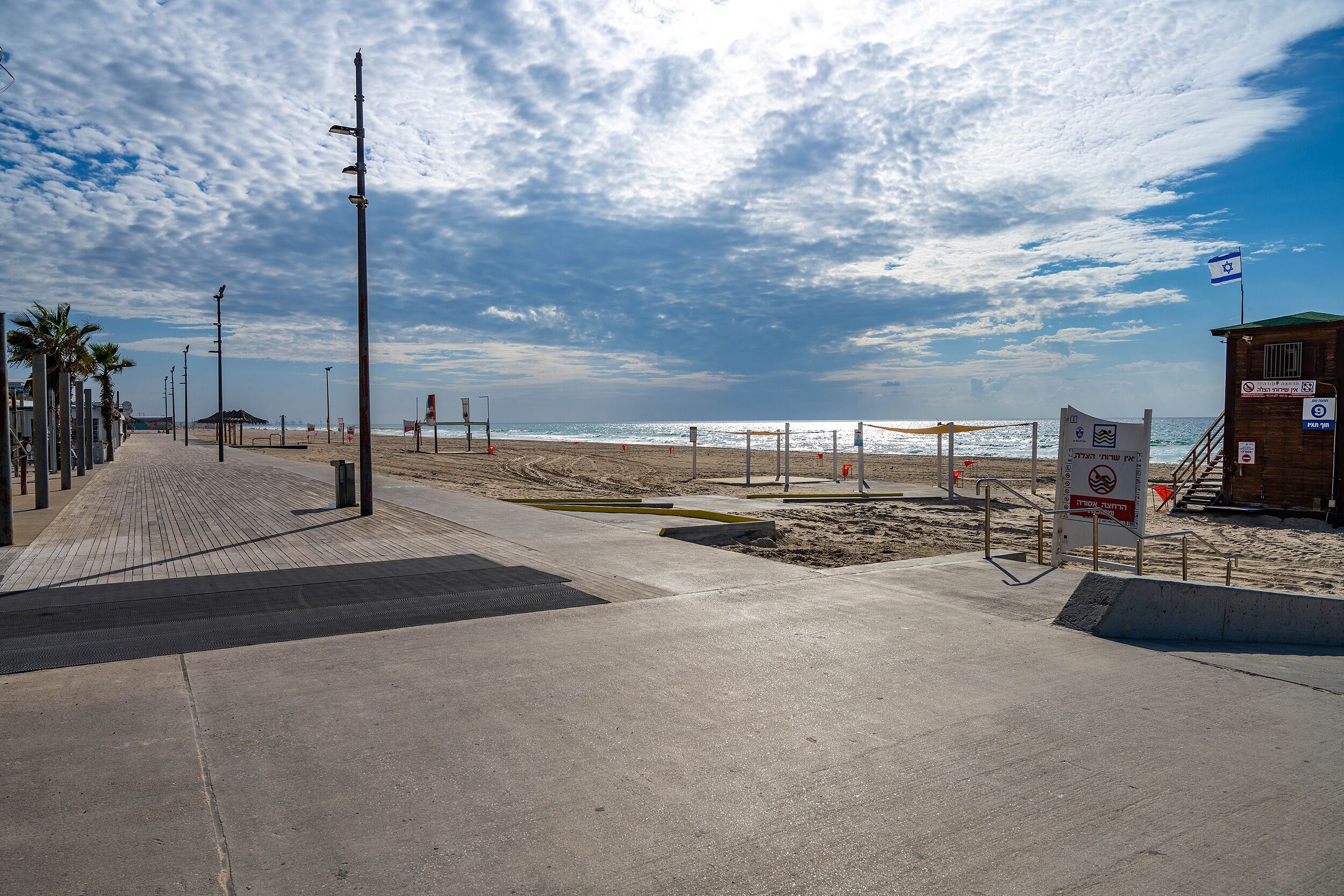 Une promenade en bord de mer bordée de palmiers, avec un poste de surveillance pour les sauveteurs et un drapeau.
