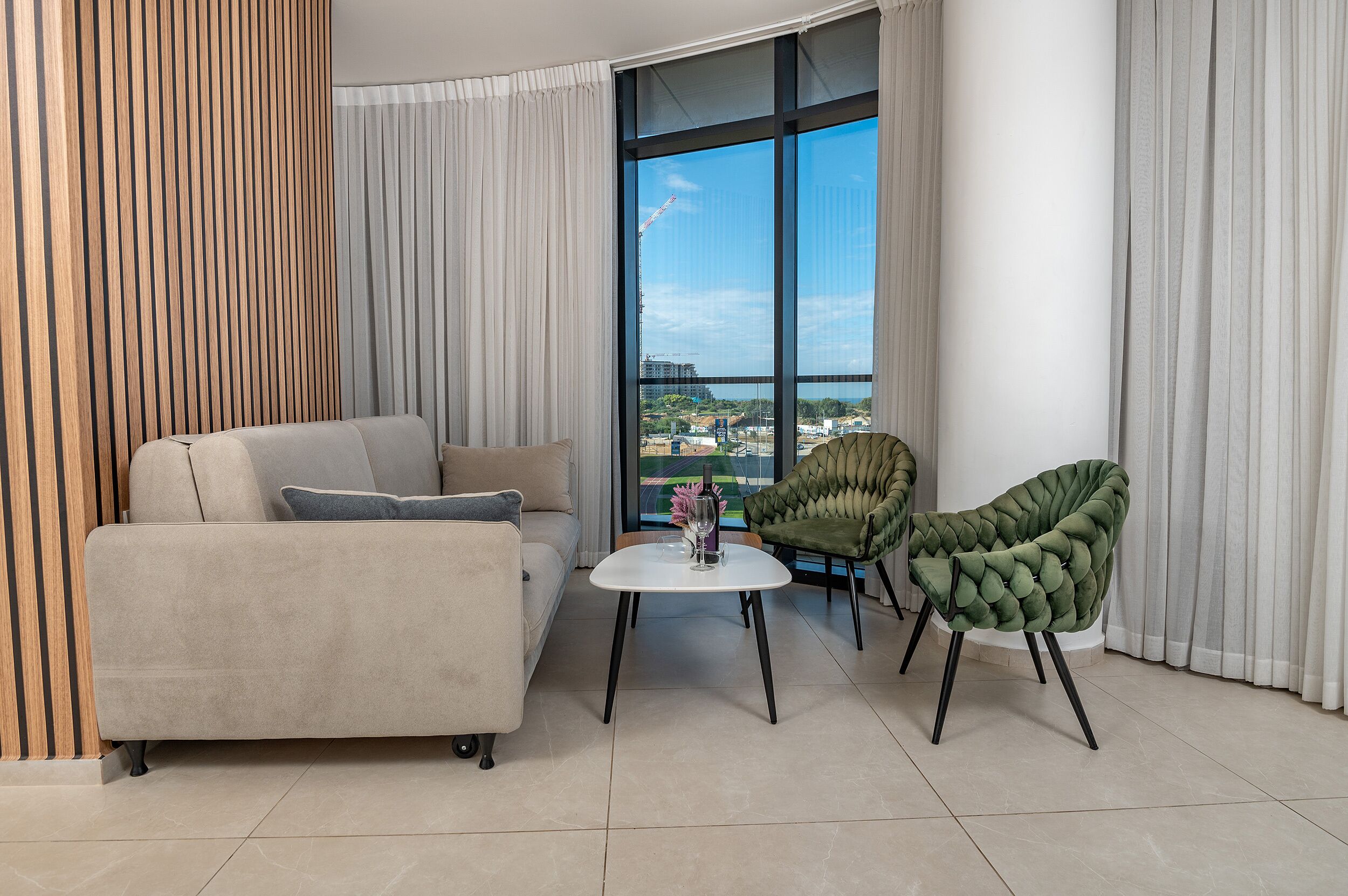 A modern living room with a sofa, two chairs, a small table, and a large window with a view of buildings.
