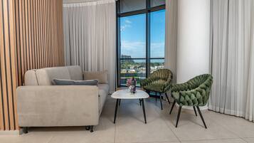 A modern living room with a sofa, two chairs, a small table, and a large window with a view of buildings.