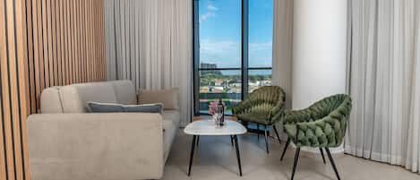 A modern living room with a sofa, two chairs, a small table, and a large window with a view of buildings.