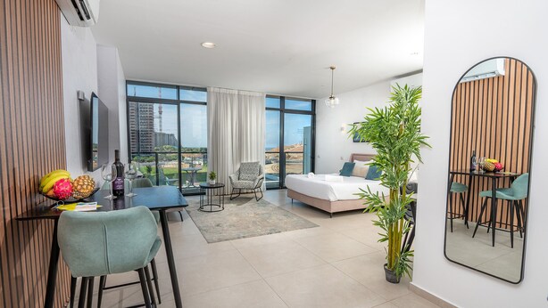 Ein modernes Hotelzimmer mit einem großen Bett, einer Essecke, einem Fernseher und einem Balkon mit Blick auf die Stadt.