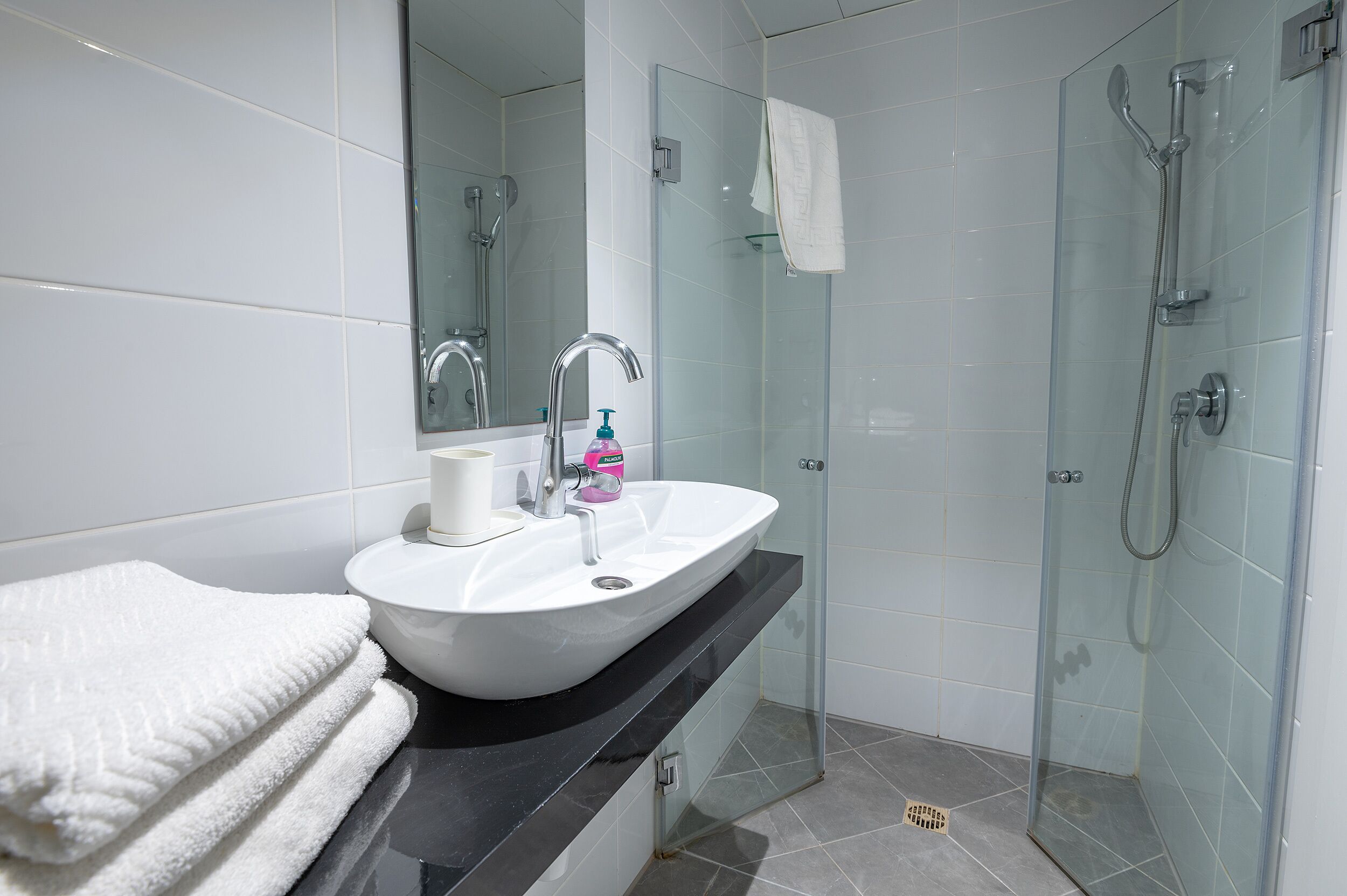 Een moderne badkamer met een wit wastafelmeubel, een douchecabine van glas en een spiegel.