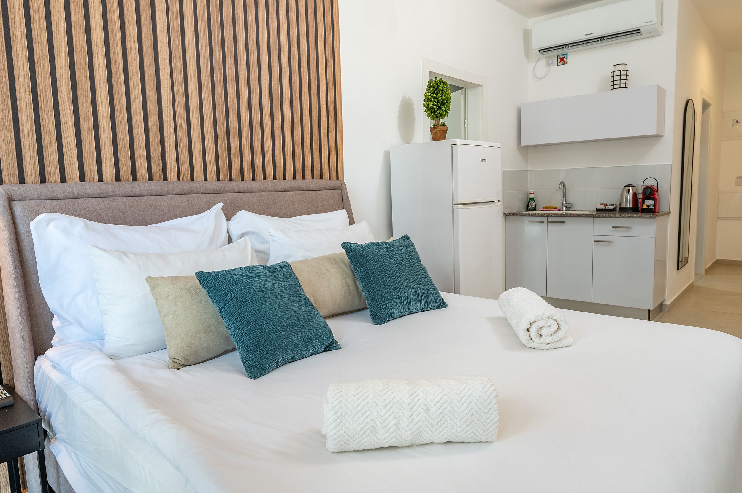 A neatly made bed with white and teal pillows, a white towel, and a wooden headboard.