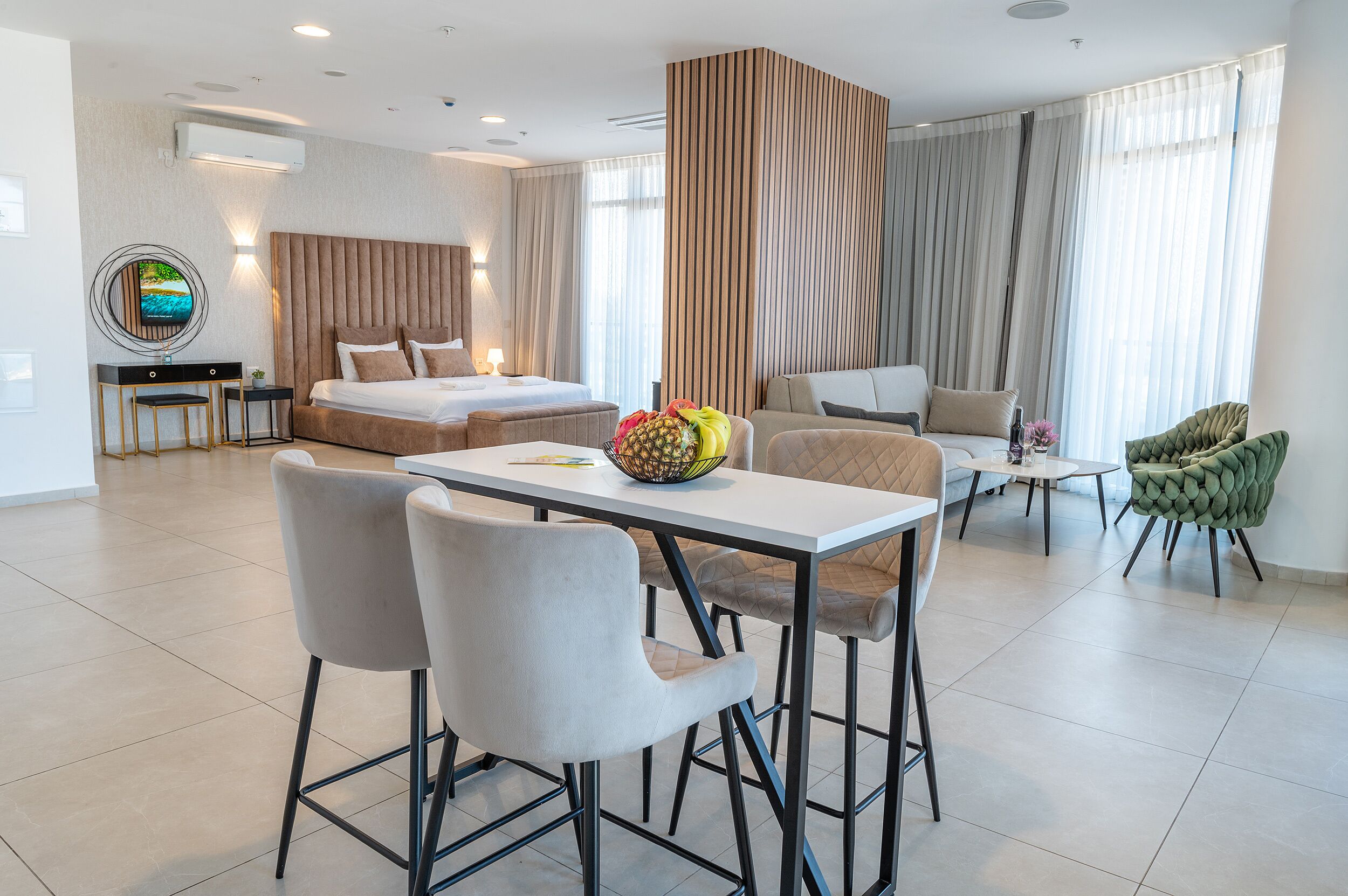 Een moderne hotelkamer met een bed, een zithoek met stoelen, een tafel en een groene fauteuil.