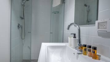A modern bathroom with a glass shower enclosure, a white sink with soap dispensers, and a mirror above the sink.