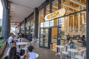 An outdoor seating area with tables and chairs, a storefront with a 'GOLDA' sign, and a view of the street. - Hi - Yam SeaView Apartments & Suites (Bat Yam)