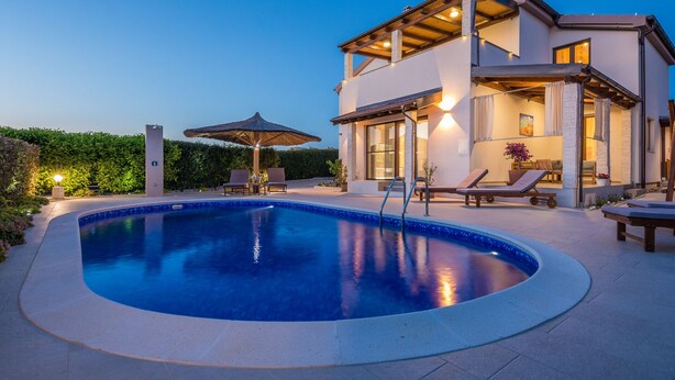 Une maison moderne à deux étages, dotée d’une piscine, d’un espace extérieur aménagé et d’un patio bien éclairé.