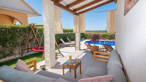 Un espace extérieur abrité avec des sièges, une piscine, des chaises longues et une balançoire.