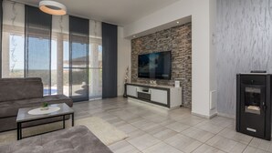 Un salon moderne avec un canapé gris, une table basse agrémentée d’une plante, un téléviseur fixé à un mur en briques et une cheminée.