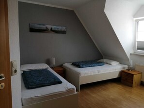 A small, sloped room with two beds, a painting on the wall, and a window.