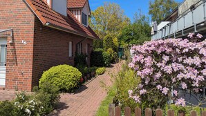 A brick house with a red-tiled roof, a number '15' on the side, and a garden with various plants and flowers. - Vacation home in Altfunnixsiel/Carolinensiel (Wittmund)