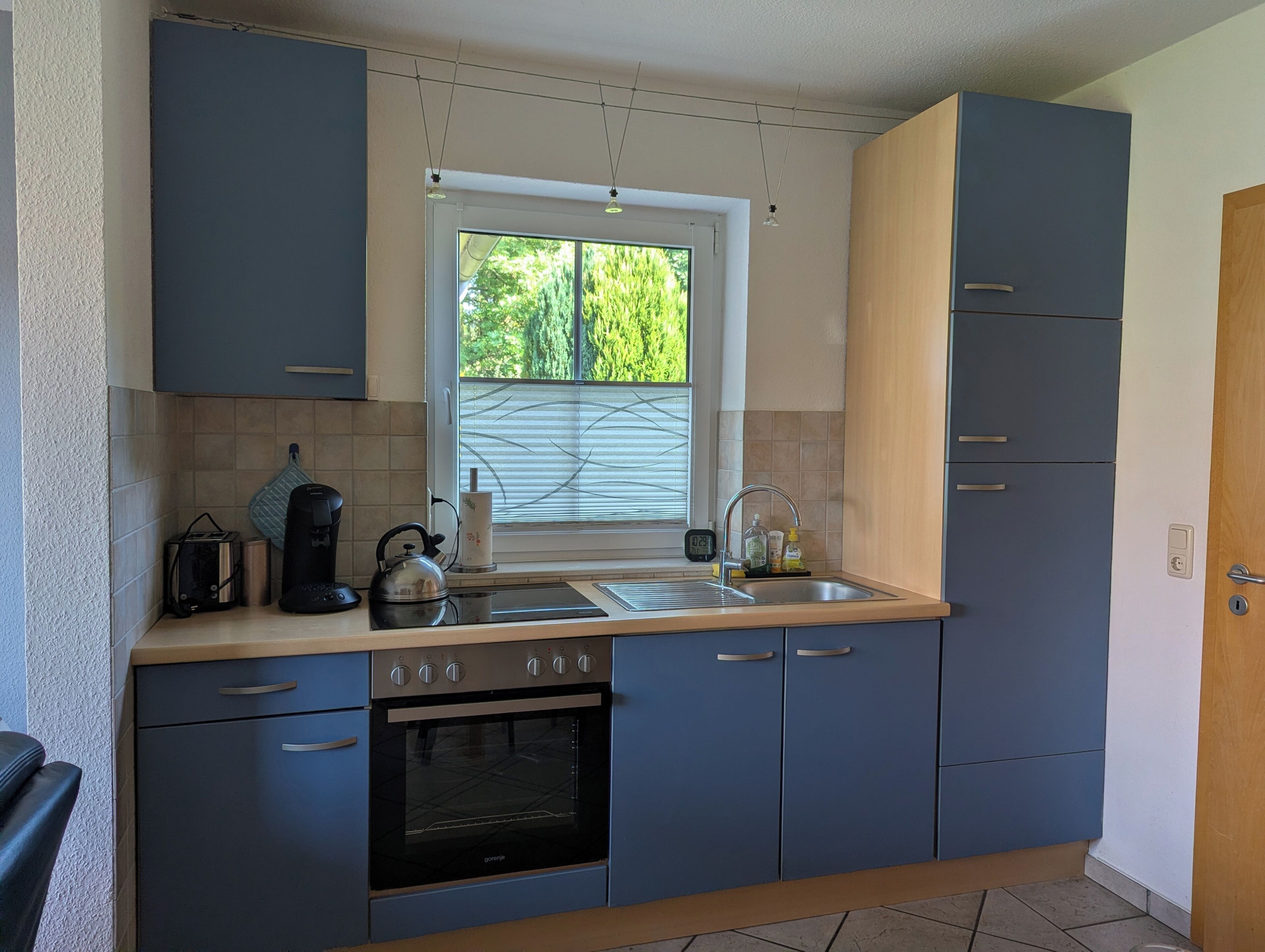 Una cucina moderna con forno integrato, lavello e una finestra con persiane.