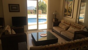 A living room with a sofa, a coffee table, a TV, and a door leading to a pool. - Fully detached Villa offers an unforgettable holiday with your family and friend (Alanya)