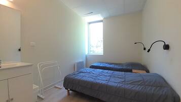 A small, well-lit bedroom with a single bed, a bedside table, a radiator, and a window providing natural light.
