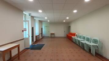 Un hall d’entrée spacieux, avec une longue rangée de chaises d’un côté, un banc en bois et une porte au fond.